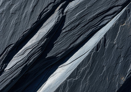 Rugged, naturally split texture of deep charcoal and bluish gray metamorphic slate rock showing fine diagonal cleavage planes and strong shadows. ideal for geology, background, or abstract design concepts.の素材
