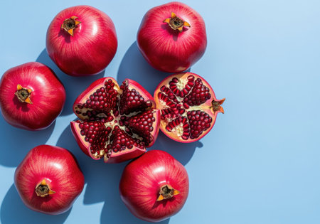 Fresh whole and halved red pomegranates arranged in a flat lay composition on a vibrant light blue surface. the exposed seeds are visible, highlighting freshness and healthy eating concepts.の素材