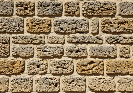 Close up of a traditional limestone cladding featuring rough hewn stones with natural pits, small fossil inclusions, and wide horizontal grout lines. the texture is rough and detailed.の素材