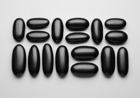Arrangement of smooth black river pebbles in a grid pattern. the stones are elongated and polished, set against a neutral background, creating a minimalist composition.の素材