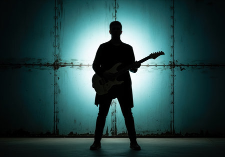 Silhouette of man standing with electric guitar against teal metal panel background. musician poses with guitar in atmospheric setting, creating a modern artistic portrait.の素材