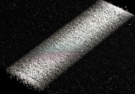 Coarse black textile fibers captured in a macro close up. a sharp diagonal beam of light illuminates fine dust particles and lint, creating a high contrast, low key abstract texture.の素材