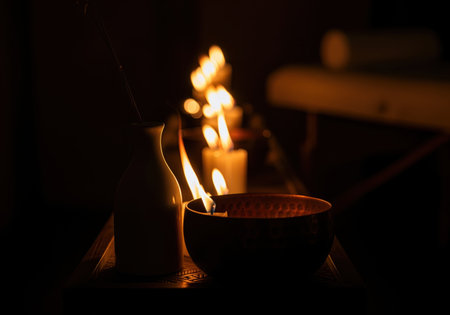 Copper singing bowl and white vase illuminated by the warm, flickering light of candles in a dark, dramatic spa setting, symbolizing relaxation and wellness.の素材