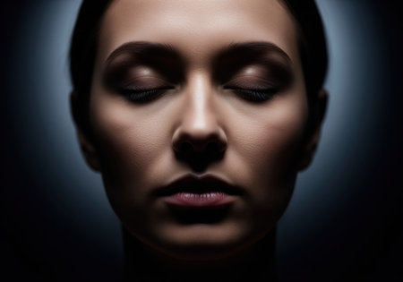 Woman face in a powerful, intimate close up portrait. dramatic low key lighting highlights the features, emphasizing deep relaxation and closed eyes against a dark background.の素材