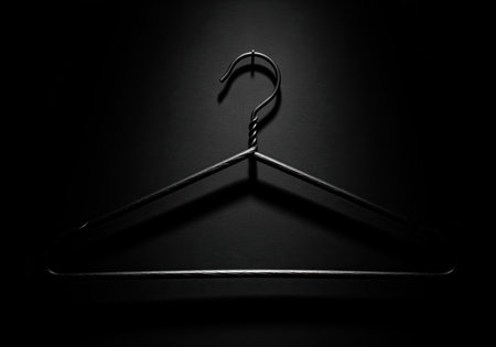 A dramatic, high contrast monochrome studio shot of a single, textured metal wire coat hanger. this minimalist image is suitable for fashion, retail, or design concepts.の素材