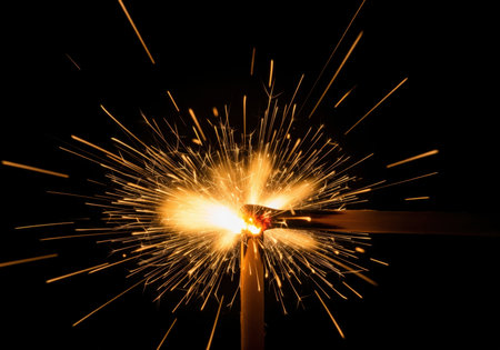 A dynamic, high intensity photograph showing a match head igniting, creating a brilliant burst of golden light and streaking sparks in the dark.の素材