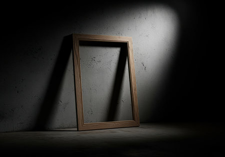 A raw, unfinished wooden picture frame stands empty, leaning against a textured concrete wall, dramatically highlighted by a single spotlight in a dark, moody setting.の素材