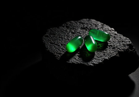 Three vibrant, translucent green softgel capsules are dramatically illuminated, resting on a rough, dark stone. perfect for illustrating health, supplements, or advanced medicine concepts.の素材