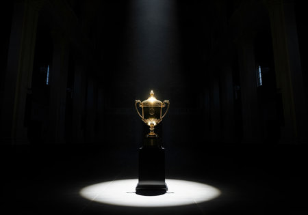 Golden championship trophy standing on a dark pedestal, dramatically illuminated by a strong, solitary spotlight in a vast, empty, dark interior hall. focus on success and victory.の素材
