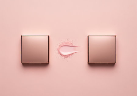 Two identical, closed, rose gold cosmetic compacts symmetrically arranged on a pink background. pink powder and creamy swatch displayed between them, highlighting texture.の素材