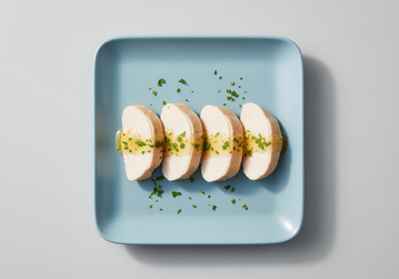 Four slices of cooked chicken breast neatly arranged on a light blue plate. the poultry is topped with a lemon herb dressing and sprinkled with fresh green herbs, presented in a clean studio setting.の素材