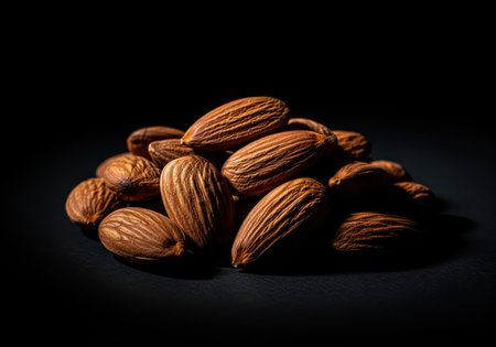 Pile of raw almond nuts, sharply focused under dramatic low key studio lighting against a deep black background. healthy snack food rich in protein and vitamins.の素材
