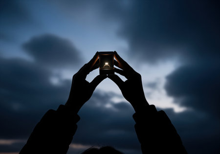 Hands in silhouette holding an illuminated engagement ring box against a dramatic, dark, cloudy sky, symbolizing love, commitment, and marriage proposal.の素材