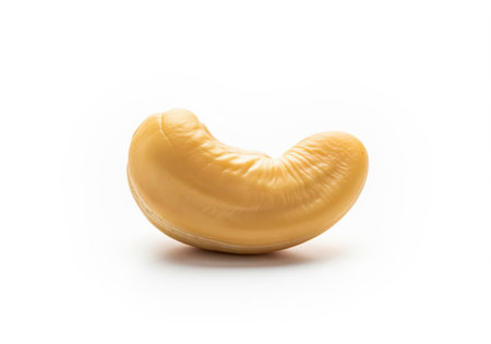Single, perfectly shaped cashew nut resting on a white surface, captured in a high resolution studio photograph. focus on healthy eating, snack food, and ingredient use.の素材