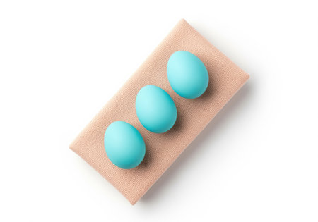 Three bright turquoise blue eggs arranged diagonally on a small piece of textured beige fabric. clean, minimalist studio shot, isolated on a white background, perfect for easter concepts.の素材