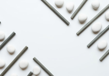 White stones and diagonal gray sticks forming a minimalist border frame on a bright white background. clean, high key, abstract geometric pattern with central copy space.の素材