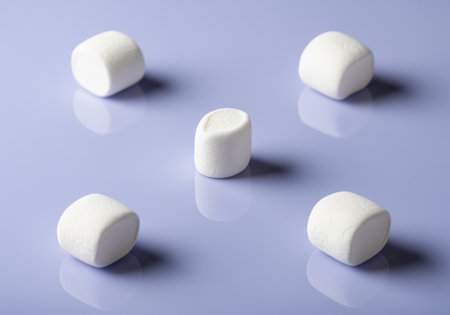 Five fluffy white marshmallows arranged symmetrically on a smooth, reflective, glossy purple surface. sweet confectionery treat, perfect for dessert, candy, or snack concepts.の素材