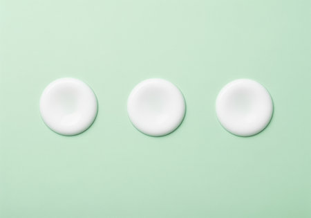 Three perfect circular drops of thick, pristine white cosmetic cream or moisturizing lotion arranged horizontally on a clean, minimalist pale green studio background. ideal for beauty and skincare concepts.の素材