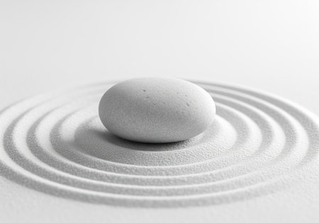 Smooth gray stone centered in a miniature zen garden of raked white sand forming concentric circles. represents balance, peace, and meditation.の素材