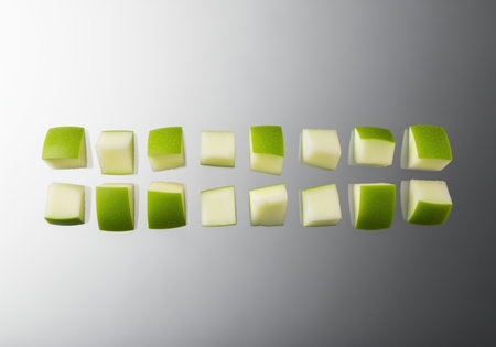 Geometrically cut, crisp green apple cubes arranged in two horizontal rows on a reflective gradient gray surface. focus on freshness, diet, and healthy food preparation.の素材