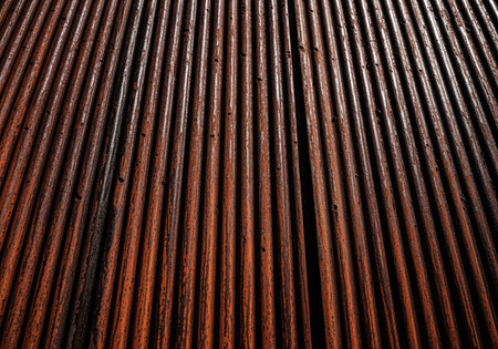 Corrugated iron sheet texture, heavily rusted and weathered, displaying deep orange and brown tones. strong vertical lines create a dramatic industrial background.の素材