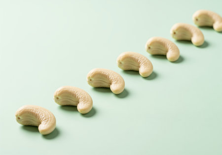 Raw cashew nut kernels, perfectly shelled and smooth, arranged in a diagonal line on a clean, light mint green background. healthy food and snack concept.の素材