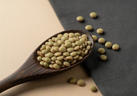 Uncooked green lentils are piled high in a dark wooden spoon, scattered across a contrasting surface. this healthy legume is a staple ingredient for nutritious vegetarian and vegan meals.の素材