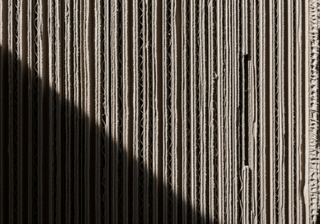 Detailed view of the raw, vertical corrugation pattern of brown cardboard, featuring deep texture and strong diagonal shadows. ideal for industrial or recycling themes.の素材