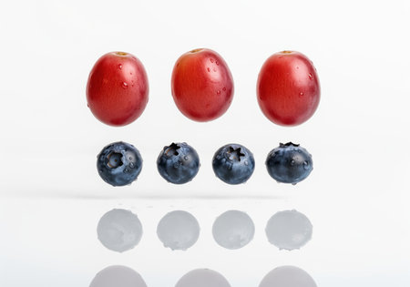 Three vibrant red grapes and four dark blueberries suspended in mid air, covered in fresh water droplets. ideal for healthy eating, diet, or juice advertising.の素材
