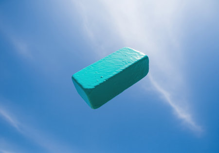 Low angle view of a bright turquoise rectangular block floating in the air. the object features a textured surface and rounded edges, ideal for design concepts.の素材