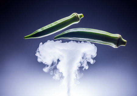 Two vibrant green okra pods are dramatically suspended mid air above a rising plume of white smoke, emphasizing freshness and culinary use.の素材