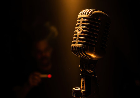 Classic vintage microphone dramatically illuminated by a warm golden spotlight against a dark, smoky background, evoking music, performance, and retro broadcast style.の素材