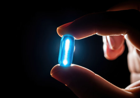 Single glowing blue capsule held between fingers against a dark background. this image symbolizes advanced medicine, pharmaceutical technology, health, and innovation.の素材