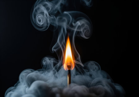 Burning matchstick centered in a studio shot, featuring a bright orange flame and dramatic, swirling white smoke trails against a solid black background. high contrast image symbolizing danger, heat, and energy.の素材