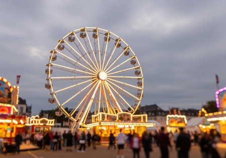 Large observation wheel illuminated with warm lights at an evening carnival. the foreground features blurred people and glowing amusement park attractions.の素材