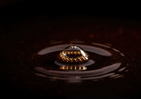 Single bubble captured in extreme close up on the surface of a viscous, dark brown liquid, reflecting golden light and creating subtle ripples. abstract texture and fluid dynamics concept.の素材