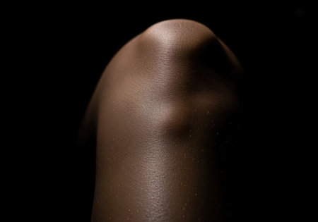 Dark skinned human knee joint and upper leg captured in a dramatic low key close up, emphasizing skin texture, contours, anatomy, and health concepts.の素材