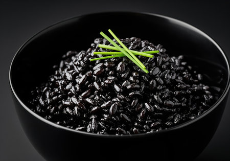Black rice cooked with squid ink, intensely focused and served in a deep black ceramic bowl, garnished with fresh green chives against a dark background. gourmet, healthy, and exotic cuisine.の素材