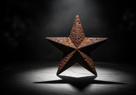 Rusted five pointed metal star standing upright, dramatically illuminated by a spotlight, casting a sharp shadow on a dark, textured surface. low key studio photography emphasizing texture and decay.の素材