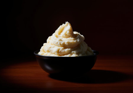 Creamy mashed potato pile served high in a dark ceramic bowl, dramatically illuminated from the side in a low key still life setting. comfort food ready for a holiday meal or dinner.の素材