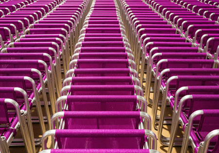 Massive stack of bright magenta folding chairs arranged in neat rows, emphasizing repetition and perspective. aluminum frames create a strong geometric pattern. suitable for themes of events, storage, or quantity.の素材