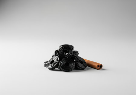 Glossy black licorice wheels piled neatly next to a brown cinnamon stick. studio product shot emphasizing sweet confectionery, flavor, and spice.の素材