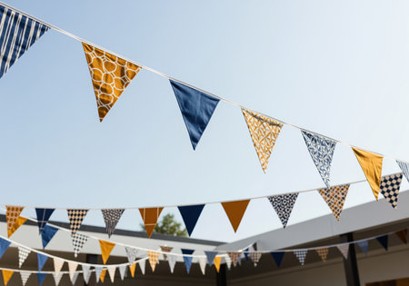 Triangular bunting flags in sophisticated blue, ochre, and white patterns strung across an outdoor setting under a clear blue sky, perfect for celebrations and events.の素材