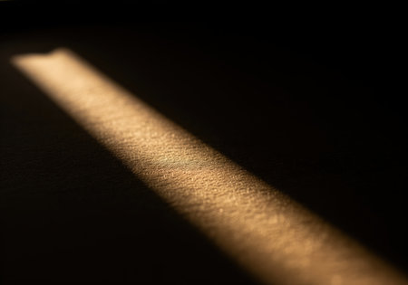 Narrow, warm light beam diagonally illuminates a textured brown surface, creating a stark chiaroscuro effect with deep shadows. focus on texture, contrast, and abstract light.の素材