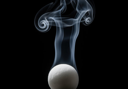 White smoke tendrils gracefully rise from a spherical mothball, illustrating the sublimation process against a stark black background. abstract vapor forms intricate curls, symbolizing transformation and mystery.の素材
