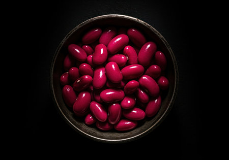 Glossy deep magenta kidney beans soaking in a dark bowl, captured from an overhead perspective with dramatic, directional lighting emphasizing their wet texture and rich color. healthy food ingredient.の素材
