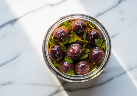 Whole black olives soaking in extra virgin olive oil with fresh oregano leaves and sea salt in a glass jar, presented on a white marble surface. perfect for mediterranean cuisine, healthy eating, and gourmet food concepts.の素材