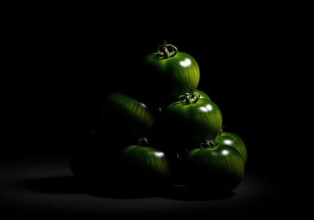 Vibrant green unripe tomatoes are artfully stacked in a pyramid formation, illuminated by dramatic low key lighting against a dark background. emphasizes freshness, healthy eating, and organic produce.の素材