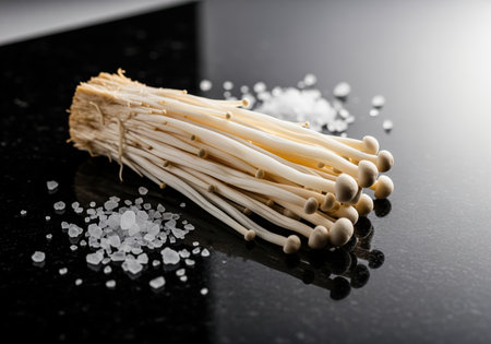 Fresh enoki mushrooms, a culinary delicacy, artfully arranged with coarse sea salt on a reflective black granite surface. ideal for gourmet cooking concepts.の素材