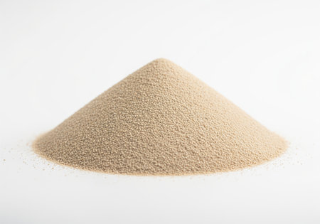 Perfectly formed conical pile of light brown fine granular material, possibly sand or powder, isolated on a clean white background. uniform texture and detailed surface for various applications.の素材